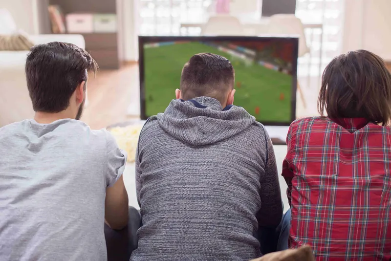 Drei Freunde schauen Fußball auf dem Fernseher im Wohnzimmer